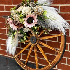 a wooden wheel with flowers and feathers on the rim next to a brick wall in front of a building