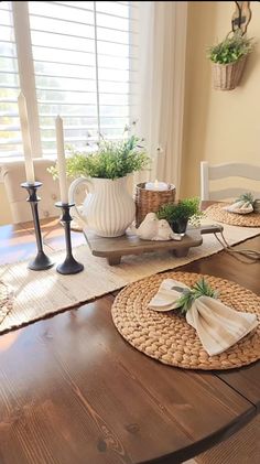 a dining room table with place mats and candles on the top, in front of a window