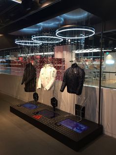 a display case filled with jackets and t - shirts in front of a window that has lights hanging from the ceiling