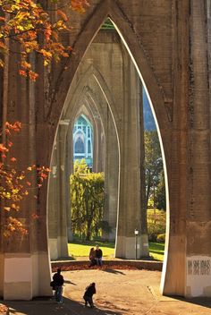 two people are walking under an arch in the middle of a park with trees and grass