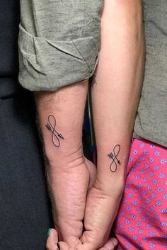 two people holding hands with tattoos on their arms