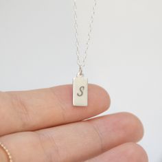 "A lovely display of your initials, or even a short word makes for a captivating look with our stylish tag pendant necklace. We will flawlessly engrave up to 2 letters on this sterling silver shiny pendant, beautifully complemented by an elegant and understated silver chain. NECKLACE DETAILS ⚬ Sterling silver rectangle tag and chain. ⚬ Rectangle measures 13.5mm x 6mm (.53\" x .23\"). ⚬ Chain in your choice of 16\", 18\", or 20\" length. ⚬ Spring ring clasp closure. ⚬ Personalized engraving of 1- Minimalist Sterling Silver Nameplate Initial Necklace, Dainty Sterling Silver Initial Necklace For Anniversary, Small Personalized Sterling Silver Necklace, Elegant Sterling Silver Hand-stamped Initial Necklace, Elegant Sterling Silver Hand Stamped Initial Necklace, Hand Stamped Rectangular Sterling Silver Necklaces, Hand Stamped Sterling Silver Rectangular Necklaces, Minimalist Sterling Silver Necklace With Hallmarks, Hand Stamped Sterling Silver Rectangular Necklace