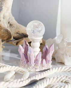 a white candle holder with pink crystals on it next to rope and driftwood pieces