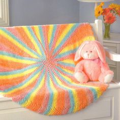 a pink stuffed animal sitting on top of a white chair next to a blanket and flowers