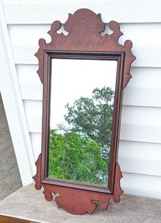 a mirror sitting on top of a wooden table next to a white house with trees in the background