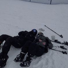 two people laying in the snow on skis