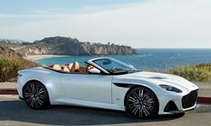 a white sports car parked in front of the ocean