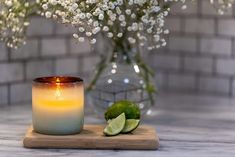 a lit candle sitting on top of a cutting board next to a vase filled with flowers