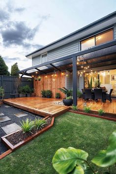 an outdoor patio with wooden decking and plants on the grass in front of it