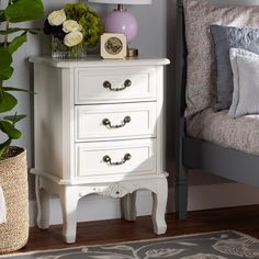 a white nightstand sitting next to a bed in a room with a plant on top of it