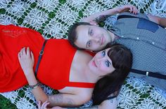 two young women laying on the ground with their arms around each other, one woman is wearing a red top