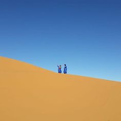 two people standing on top of a sand dune