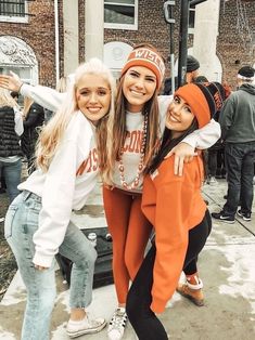 three girls are posing for the camera in front of a building with people standing around