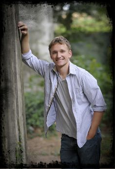 a young man leaning against a wooden pole smiling at the camera with his arm up