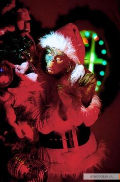 a man dressed as santa clause standing next to a christmas tree in front of a clock