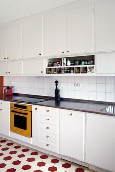 a kitchen with white cabinets and black counter tops, yellow stove top oven and red floor tiles