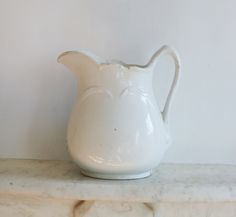 a white pitcher sitting on top of a marble shelf