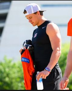 a man in black shirt and white cap holding an orange jacket with water bottle on it