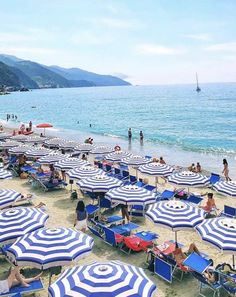 many people are on the beach with blue and white umbrellas in front of them