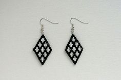 a pair of black and white beaded earrings hanging from silver hooks on a white surface