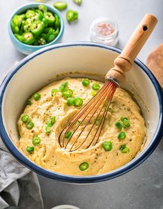 a bowl filled with hummus and green peppers next to a wooden whisk