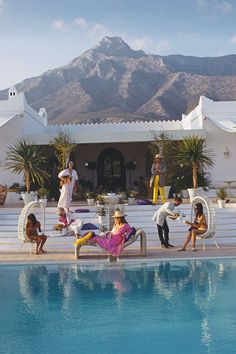 some people are sitting by the edge of a swimming pool with mountains in the background