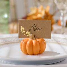 an orange pumpkin sitting on top of a white plate with a name card attached to it