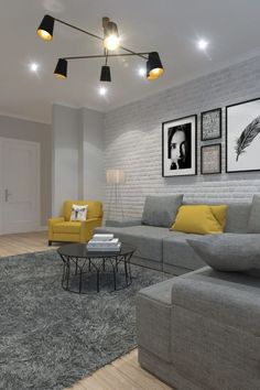 a living room with grey couches and yellow chairs in front of a white brick wall