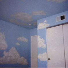 an empty room with clouds painted on the wall and door to another room in it