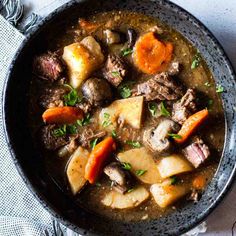 a bowl filled with stew and vegetables on top of a white table cloth next to a spoon