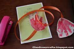 a handprinted heart on a card next to a pink ribbon and a clipboard