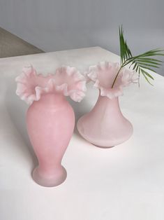 two pink vases with flowers in them on a white table top, one has a green plant