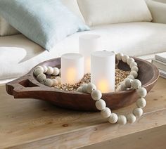 three candles are sitting in a bowl on a wooden tray with shells and beads around it