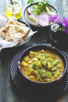 two bowls of food on a table with some bread and flowers in the bowl next to it