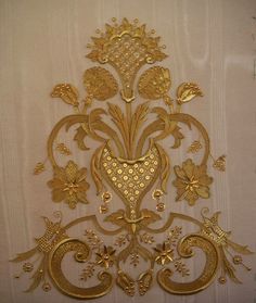 an ornate gold wall hanging on the side of a white curtain with flowers and leaves