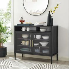 a black cabinet with plates and cups on it next to a potted plant in front of a round mirror