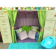 an office cubicle with green curtains and pillows on the floor next to filing cabinets