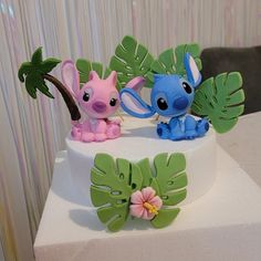 two small figurines sitting on top of a cake decorated with leaves and flowers