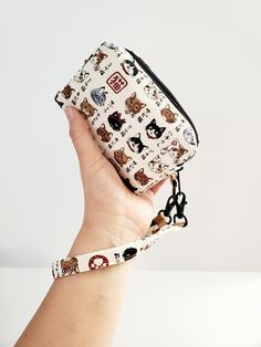 a hand holding a small purse with cats all over it and the strap around it