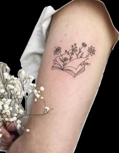 a woman's arm with flowers and an open book tattoo