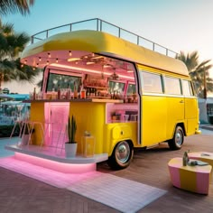 a yellow and pink bus parked next to a palm tree in front of a building