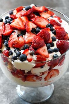 a dessert with strawberries, blueberries and cream in a glass dish on a table