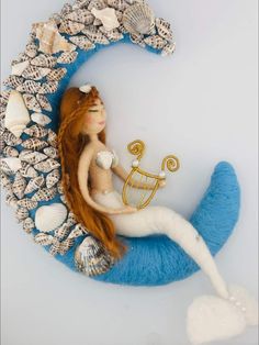 a mermaid doll is sitting on the moon with shells around her and holding a harp