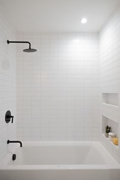 a white tiled bathroom with black fixtures and shelves on either side of the bathtub