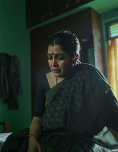 a woman in a sari sitting on a bed looking at the camera with her eyes closed