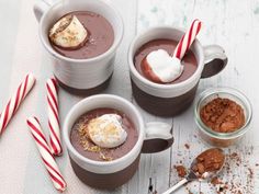 three mugs filled with hot chocolate and marshmallows on top of a table