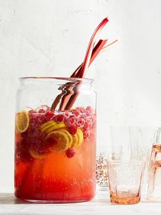 a pitcher filled with liquid next to glasses and strawberries on the side, including raspberries