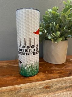 a golf themed tumbler sitting on top of a wooden table next to a potted plant