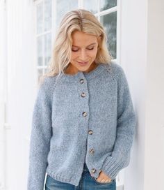 a woman standing next to a window wearing a blue sweater and jeans