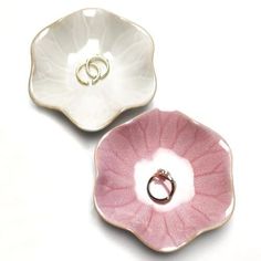 two pink and white flower shaped dishes with wedding rings in the middle one on top